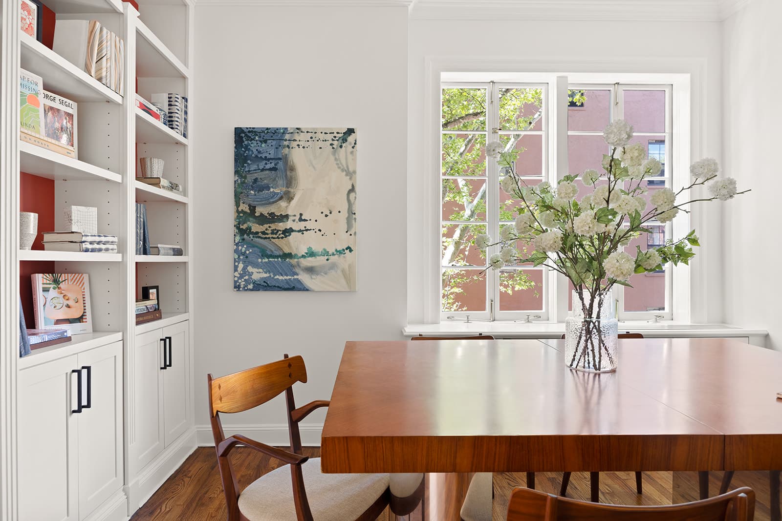 A walnut dining table under a tall window, with built-in shelves beside it