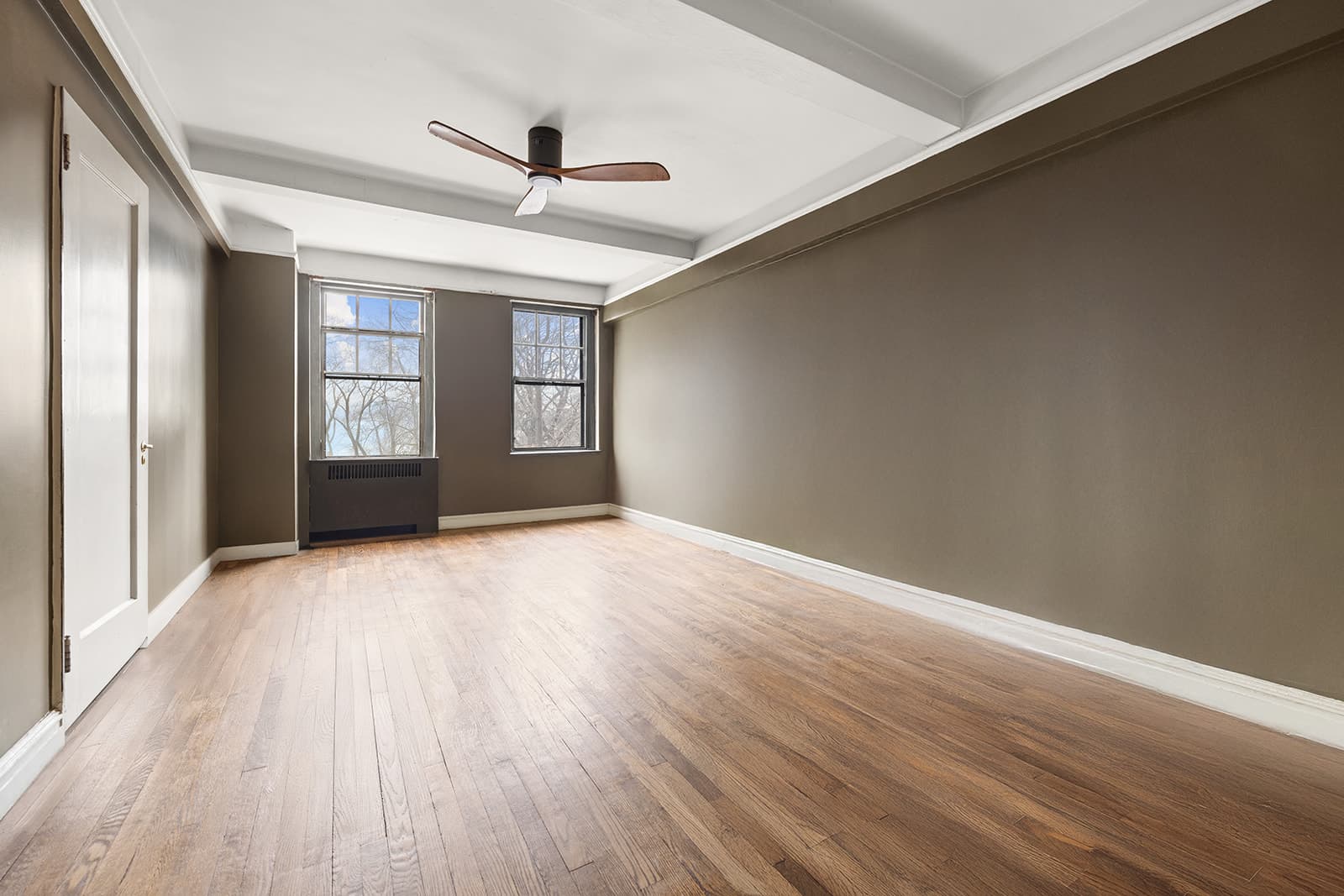 An empty bedroom with windows onto the trees of Riverside Park